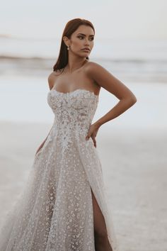 a woman standing on the beach wearing a white dress with silver sequins and high slit