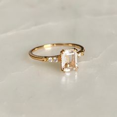 a gold ring with an emerald cut diamond in the center on a white marble surface