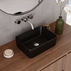 a black square sink sitting on top of a wooden counter next to a round mirror