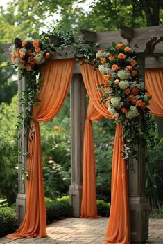 an outdoor wedding ceremony with orange drapes and flowers on the arbor, surrounded by greenery