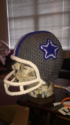 a crocheted football helmet with a blue star on the side sits on a table in front of a window