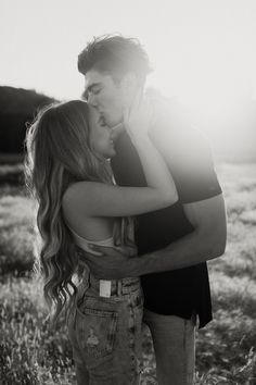 a man and woman kissing in a field with the sun shining down on them behind them