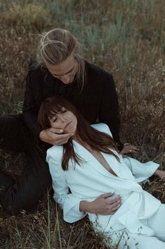 a man and woman laying on the ground in tall grass with their arms around each other