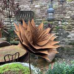 a large metal flower sitting on top of a table next to a chair and potted plant