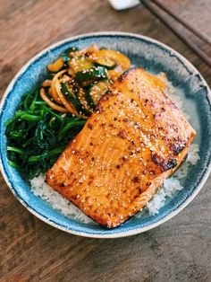 a blue and white plate topped with salmon, rice and vegetables next to chopsticks