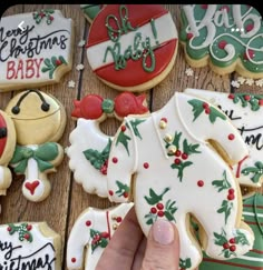 a hand is holding a decorated christmas baby cookie in front of some cookies on a table