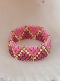 a pink and gold beaded bracelet sitting on top of a white table next to a vase