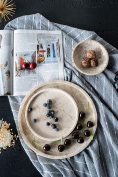 an open magazine on a table next to two plates with berries and nuts in them