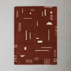 a red rug with white lines and shapes on the bottom, in front of a gray background