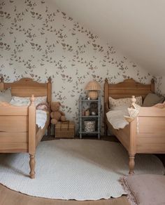 two wooden beds sitting in a bedroom under a slanted ceiling with floral wallpaper