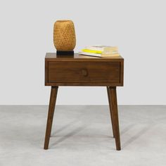 a small wooden table with a vase and books on it's top, against a gray background