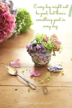 flowers in a vase with a spoon on the table next to it and a quote