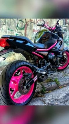 a pink and black motorcycle parked in front of a graffiti covered wall