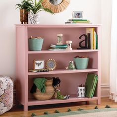 a pink bookcase with baskets and plants on top