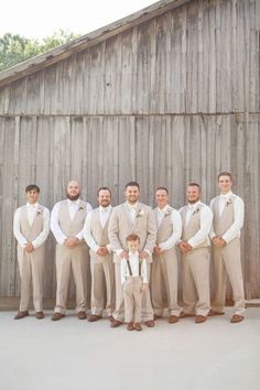 a group of men standing next to each other in front of a wooden barn wall