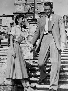 a man and woman holding hands walking up some steps in front of an old church