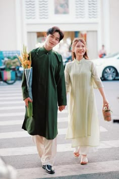 a man and woman walking across a cross walk holding an orange flower in their hand