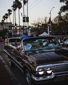 an old car is parked on the side of the road with other cars behind it