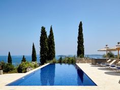 an outdoor swimming pool with lounge chairs and umbrellas overlooking the ocean in front of a house