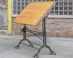 a wooden table sitting on wheels in front of a brick wall with windows behind it