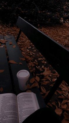 an open book sitting on top of a wooden bench next to a cup of coffee