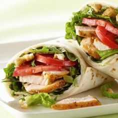 two wraps filled with meat, lettuce and tomatoes on a white platter