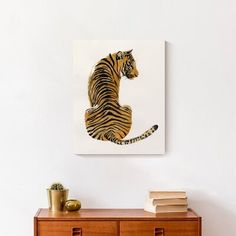 a tiger sitting on top of a wooden dresser next to a wall mounted art piece