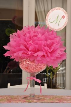 a vase filled with pink tissue flowers on top of a white table cloth covered table