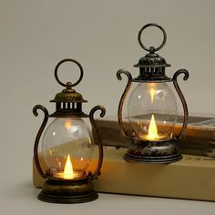 two glass lanterns sitting on top of a book next to each other with candles in them