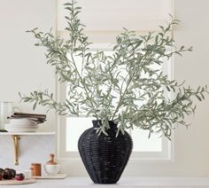 a black vase filled with green leaves sitting on top of a counter next to a window