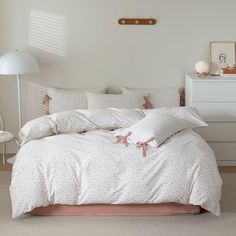 a bed with white sheets and pink pillows in a room next to a lamp on a dresser