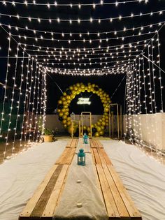 a wooden table topped with a lantern and some white cloth covered tables under string lights