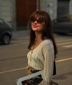 a woman is standing on the street with her hand in her pocket and holding a book