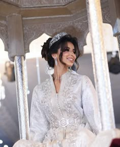 a woman wearing a tiara is sitting on a white gazebo smiling at the camera