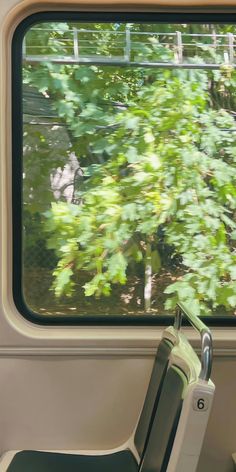 an empty seat in front of a window on a train with trees out the window