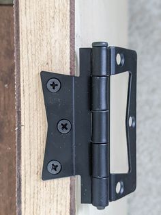 a close up of a black door hinge on a wooden door with two screws