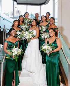 a group of women standing next to each other in front of a staircase holding bouquets