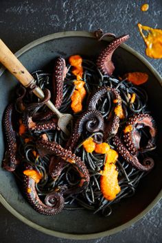 an octopus pasta dish with orange peels and sauce in a bowl next to a wooden utensil