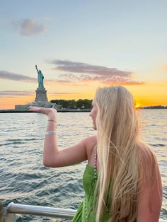 a woman in a green dress is looking at the statue of liberty from a boat