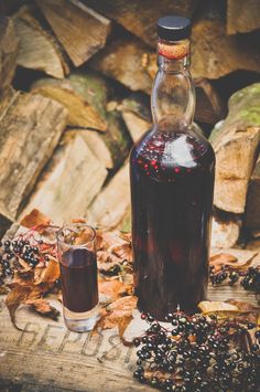 a bottle of liquid sitting next to a glass filled with blackberries on top of leaves