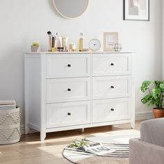 a white dresser sitting in a living room next to a mirror and potted plant