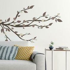 a white couch sitting next to a wall with a branch painted on it's side