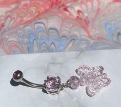 a pair of dangling belly rings with pink crystal flowers on them sitting on a marble surface