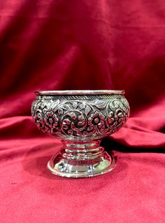 an ornate silver bowl sitting on top of a red cloth covered table with a pink background