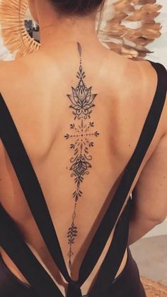 the back of a woman's neck with an intricate tattoo design on her lower back