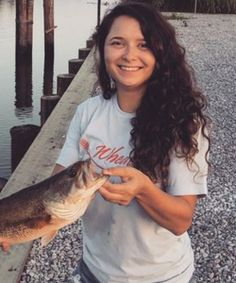 a woman is holding a fish on the dock