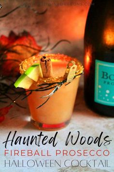 a halloween cocktail with an apple and cinnamon garnish on the rim next to a bottle of booze