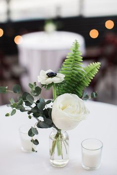 two vases with flowers and greenery sit on a table in front of candles