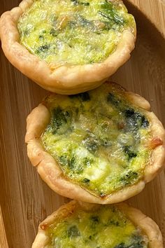 three small quiche pies sitting on top of a wooden tray next to each other