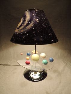 a lamp that is sitting on top of a glass table with planets around it and a black shade